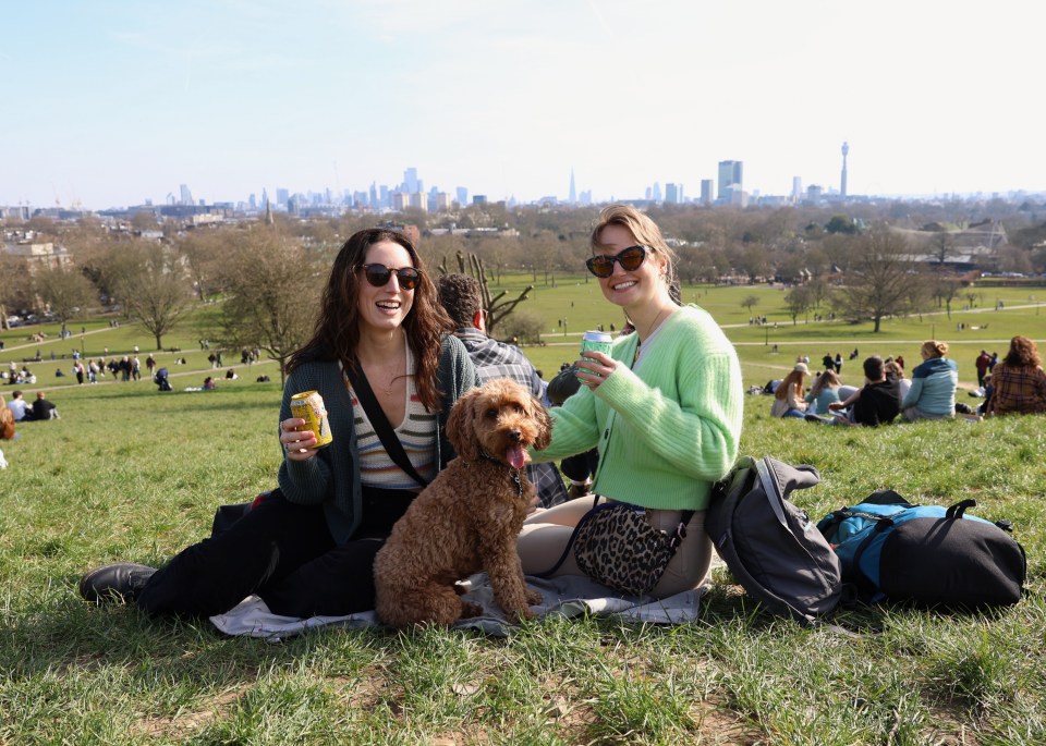 Two women and their dog enjoy a sunny day in Primrose Hill, London.