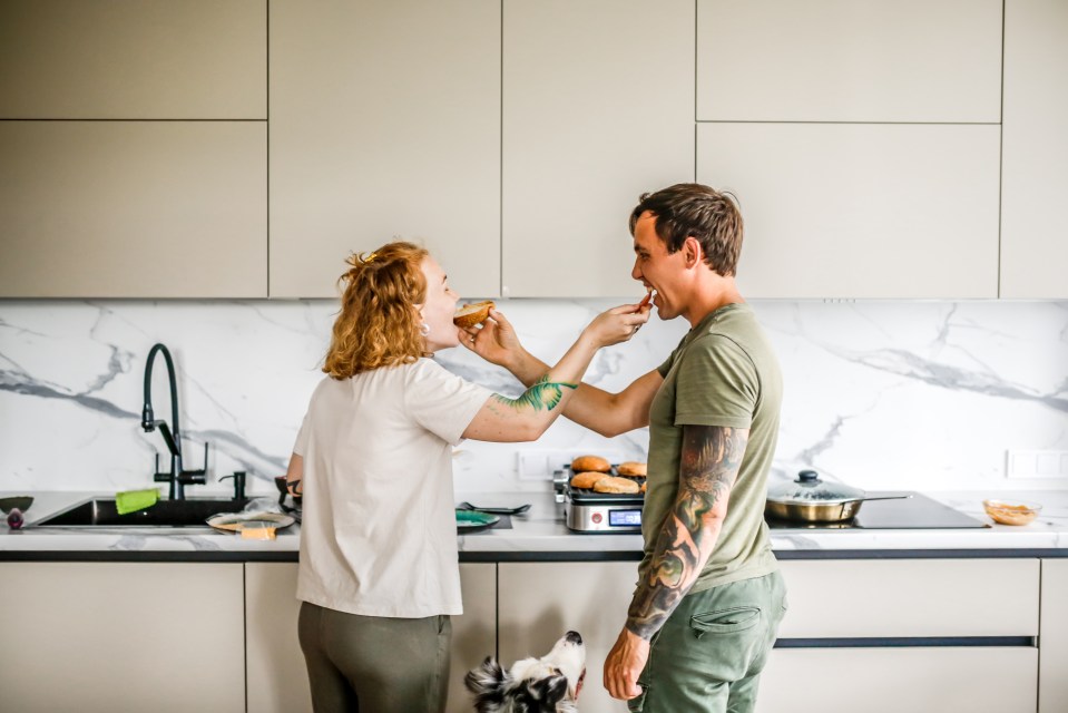 A tattooed couple prepares food together in their kitchen.
