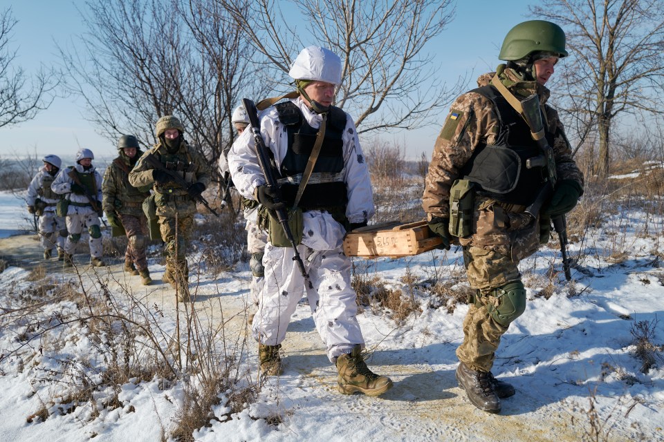 Ukrainian infantry soldiers carrying weapons and ammunition in a snowy landscape.