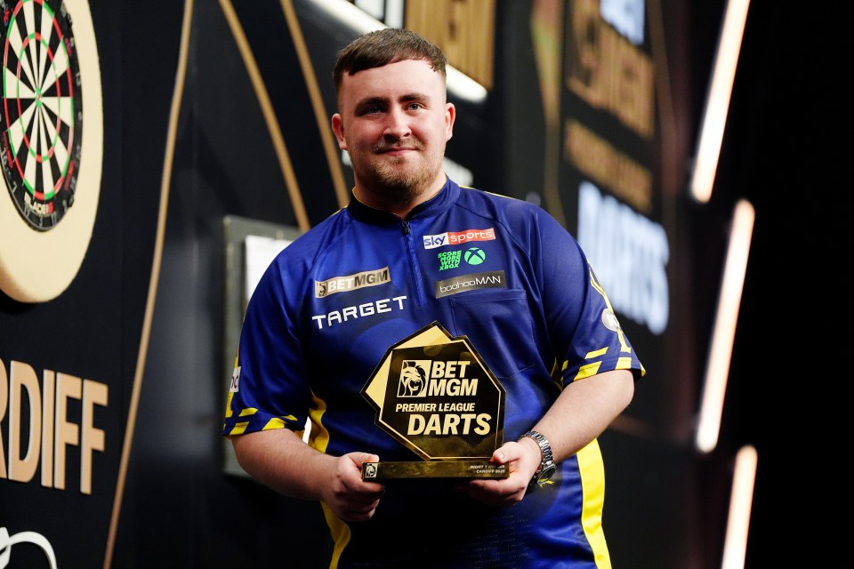Luke Littler holding a Premier League Darts trophy.