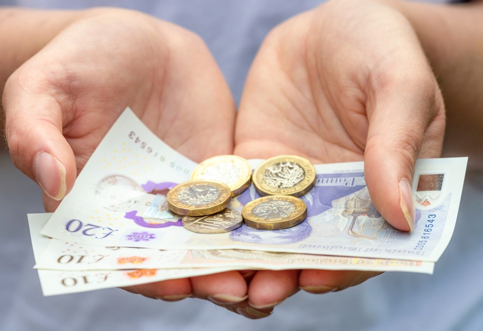 Hands holding British ten and twenty pound notes and coins.