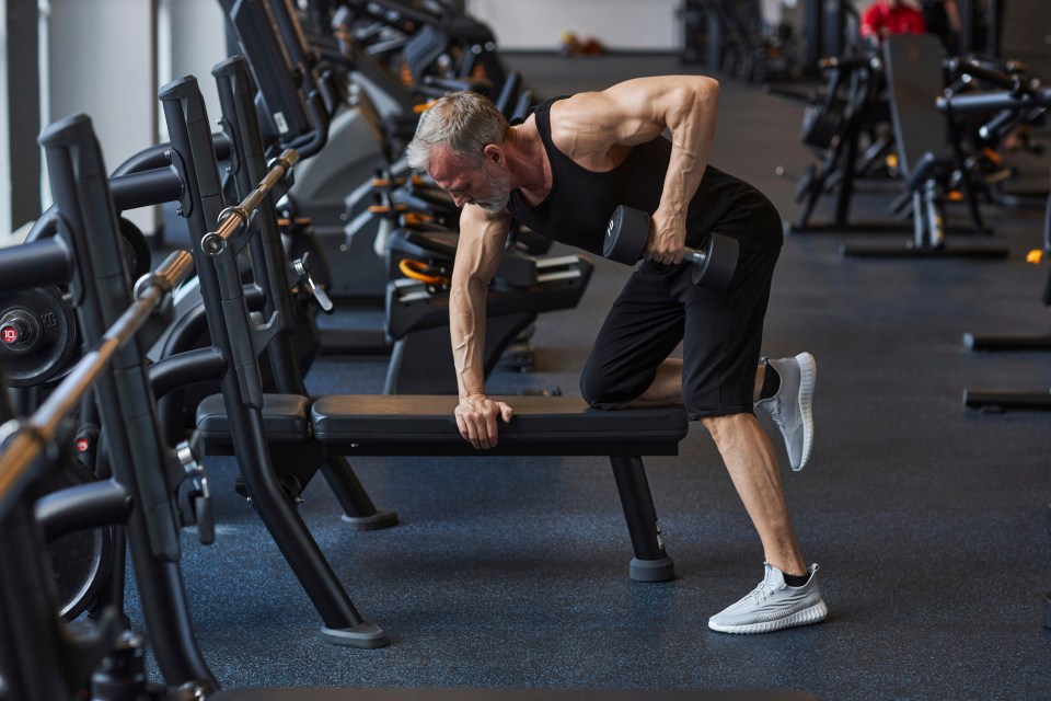 Mature man doing dumbbell rows in a gym.