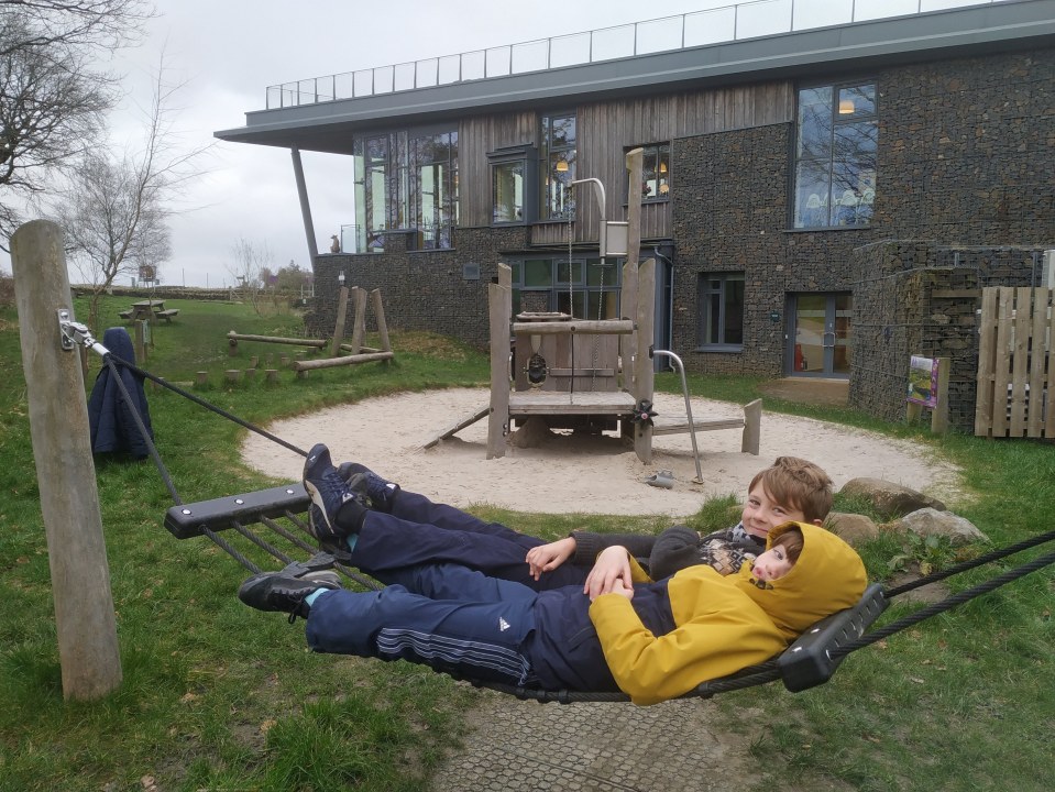 Two children relaxing in a rope hammock at The Sill hostel.