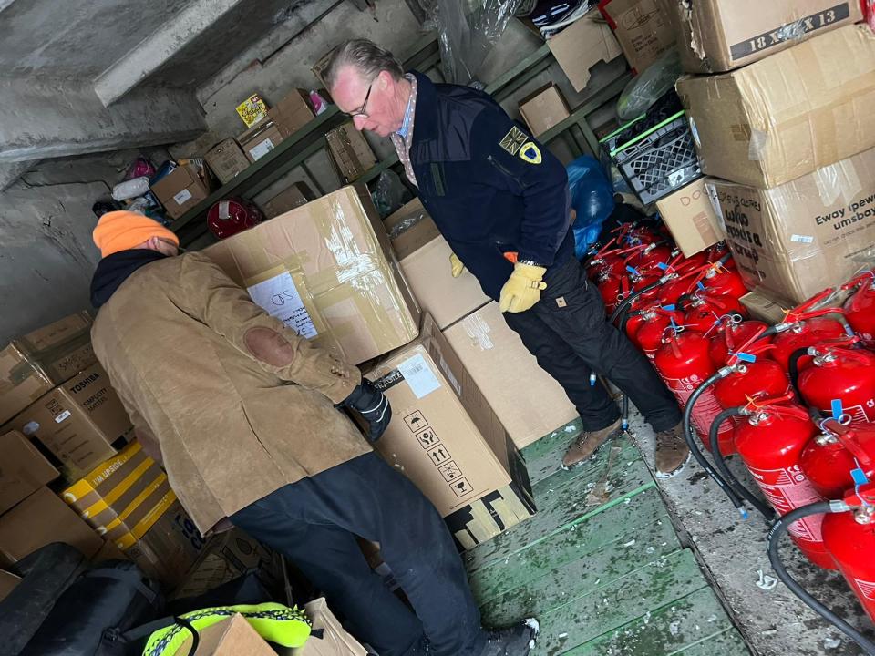 Two men examining boxes and fire extinguishers in a warehouse.