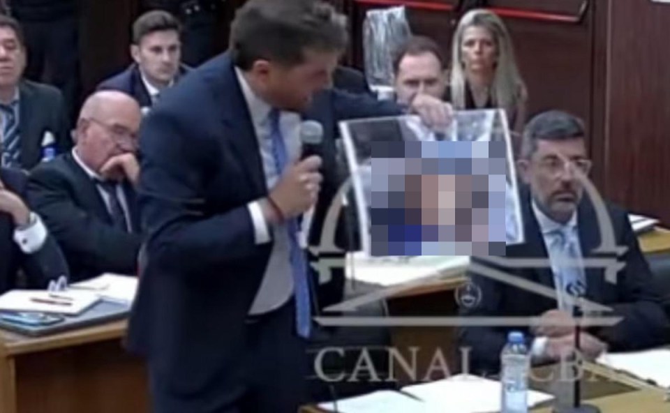 A man holding a partially obscured photo in a courtroom.