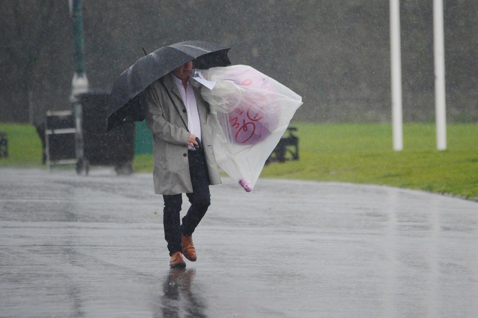 Person walking in heavy rain with an umbrella and a plastic bag.