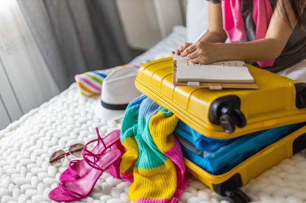 Woman packing a yellow suitcase and writing a packing list.