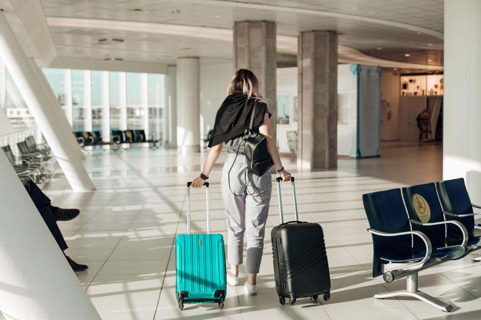 Woman pulling two suitcases through an airport terminal.