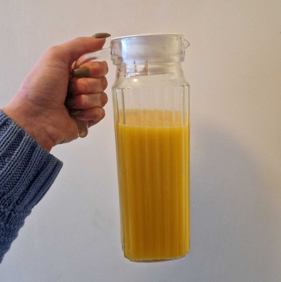 Hand holding a glass pitcher of ginger juice.