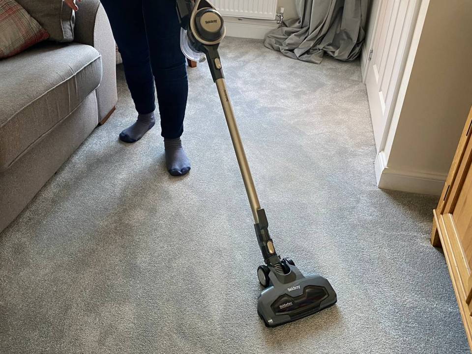 Person vacuuming carpet with a Beldray Airgility cordless vacuum.