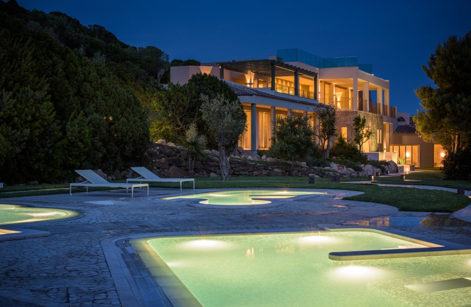 Night view of a luxury resort with illuminated pools and a modern building.