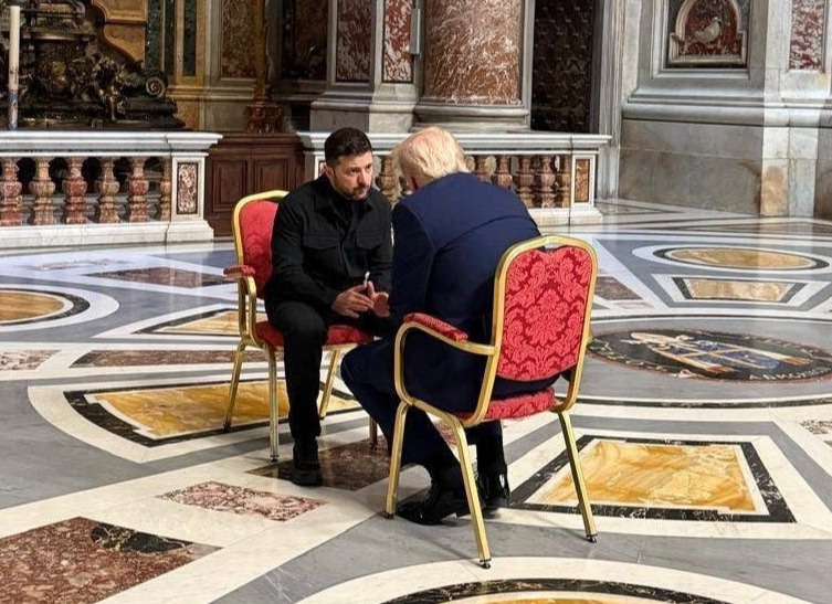 Two men seated in chairs in a ornate marble room, in conversation.
