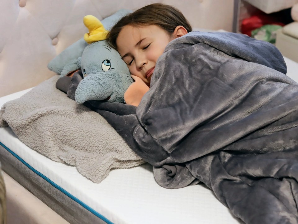 Girl sleeping on a mattress with a stuffed elephant.