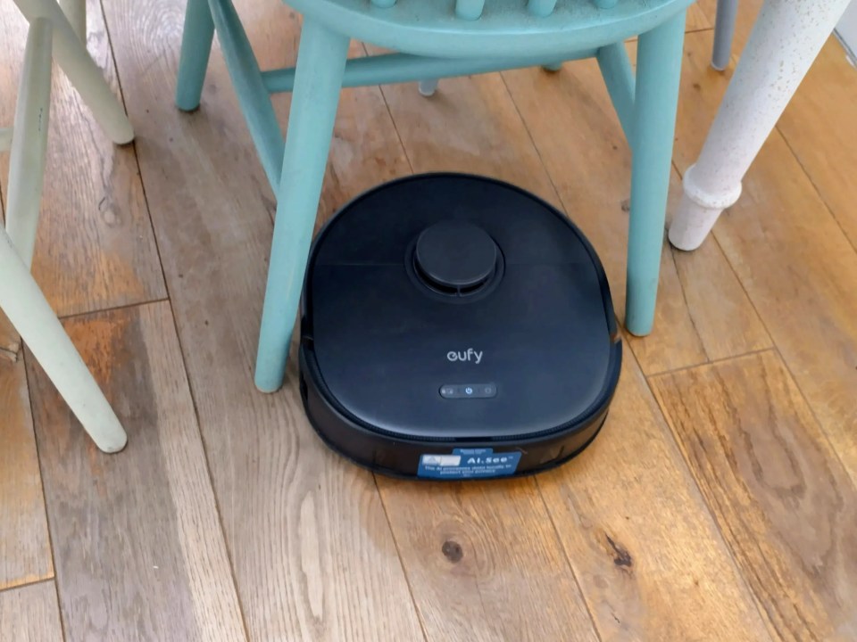 Eufy X10 Pro Omni robot vacuum cleaner on hardwood floor under chairs.