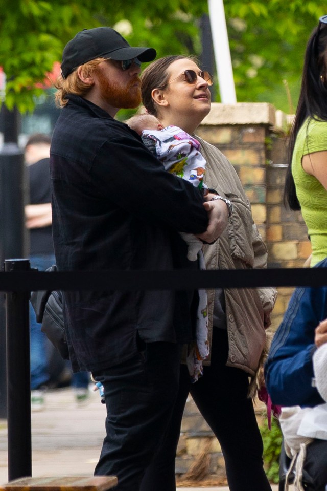 Rupert Grint holding his newborn baby while out with his partner and daughter.