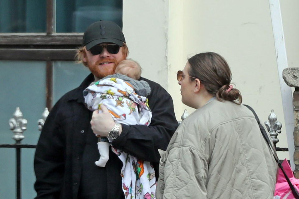Rupert Grint holding his newborn baby while out with his partner and daughter.