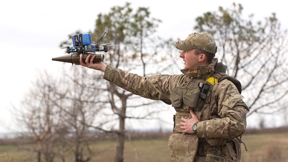 A soldier holding a drone modified for carrying a projectile.