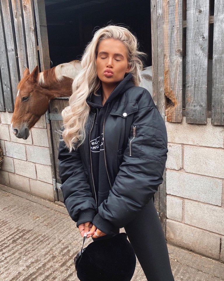 Woman in black jacket with horse in background.