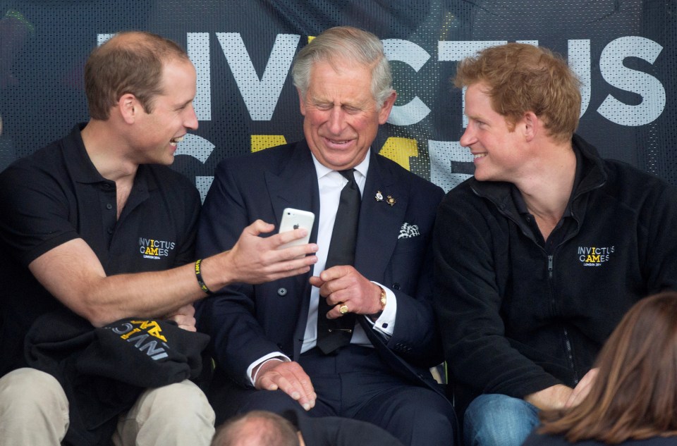Princes William, Charles, and Harry looking at a mobile phone.