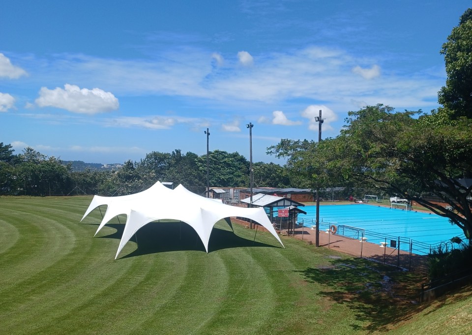 White tent on grassy field next to a swimming pool.