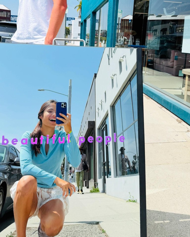 Woman taking a selfie in front of a mirror reflecting a street scene.