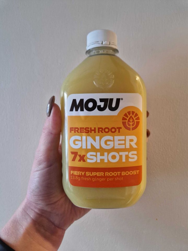 A hand holding a bottle of Moju Fresh Root Ginger Shots.
