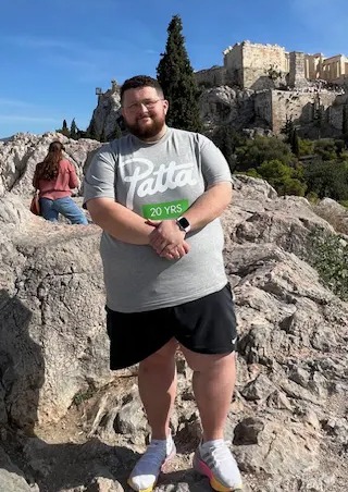 Man standing on rocks in front of the Acropolis in Athens.