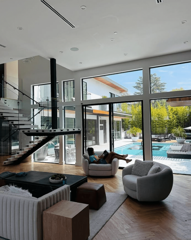 Person relaxing in a chair in a modern living room overlooking a pool.