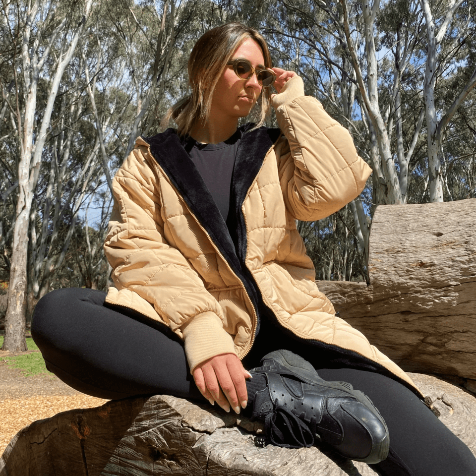 Woman in a tan jacket sitting on a log.