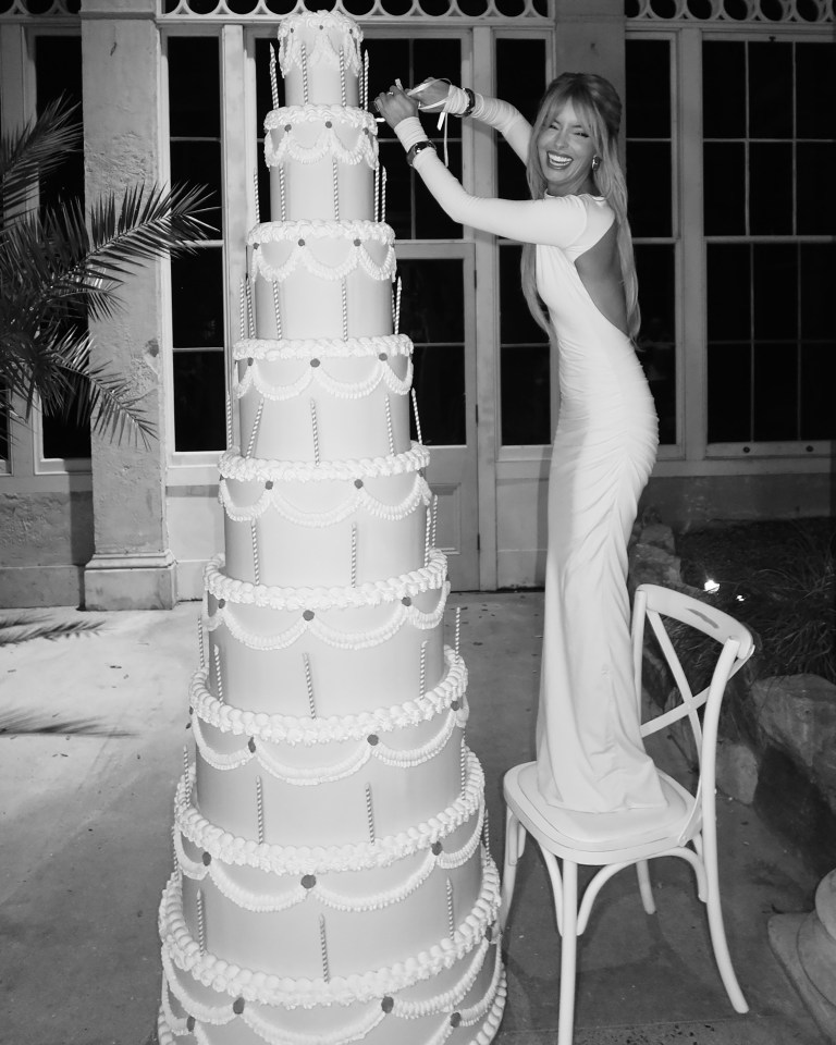 Woman in white dress cutting a large tiered wedding cake.
