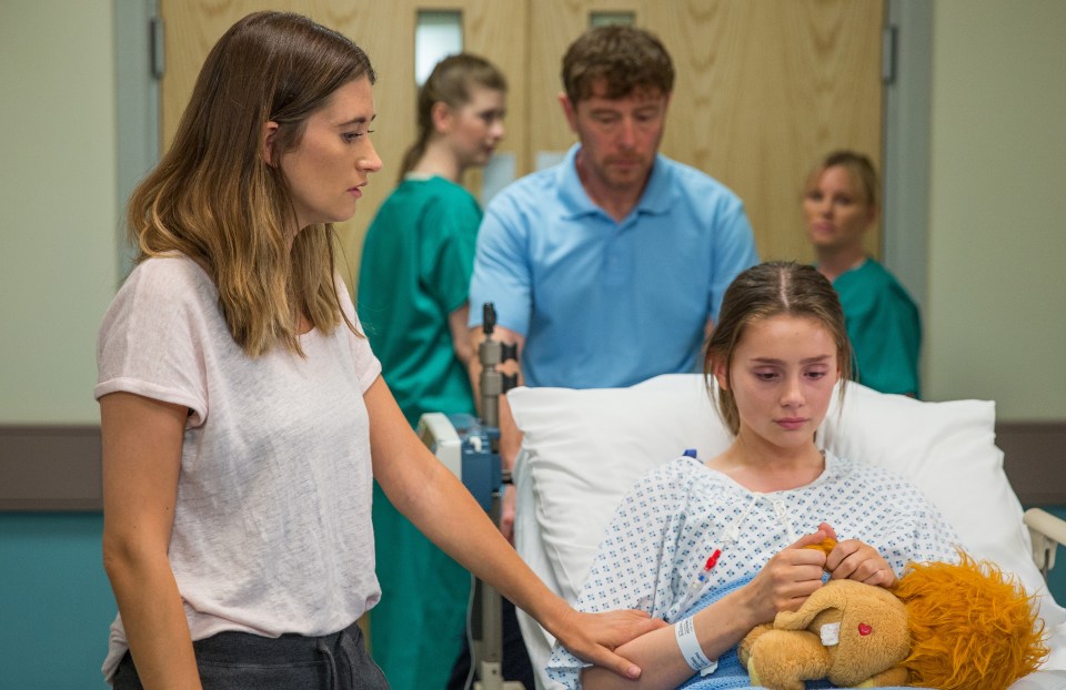 A worried woman comforts a young girl lying in a hospital bed.