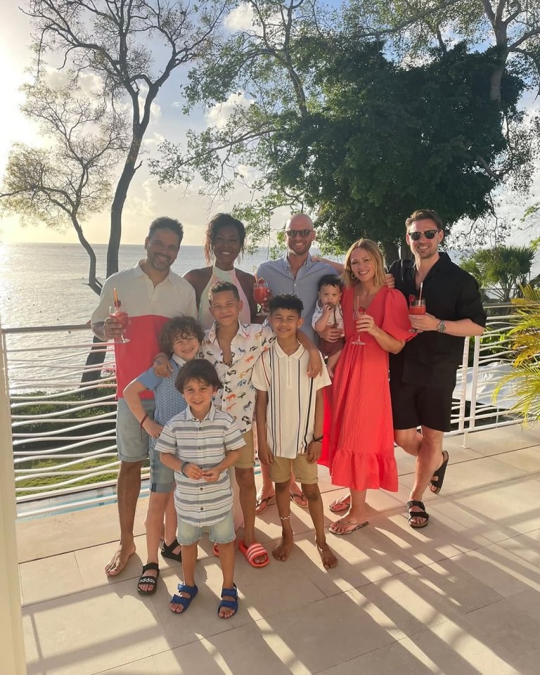 Group photo of two adults and six children with three other adults in the background, all smiling on a patio overlooking the ocean.