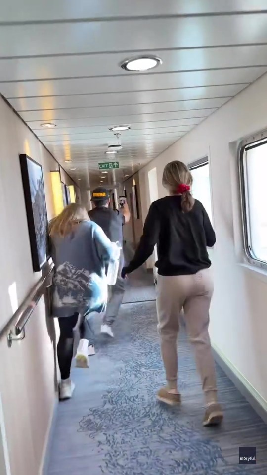 Passengers hurrying down a cruise ship hallway during rough seas.