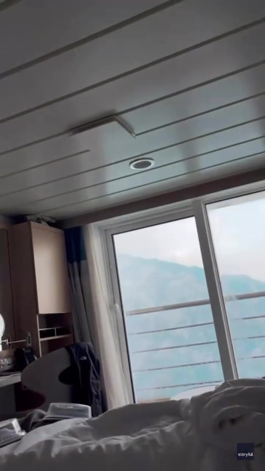 Cruise ship cabin with large window showing rough seas.