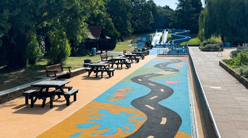 Picnic tables and a playground area next to a swimming pool with slides.