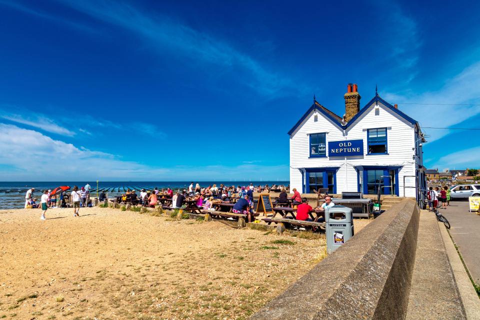 The Old Neptune pub on a beach in Whitstable, Kent, UK, with many people sitting at outdoor tables.