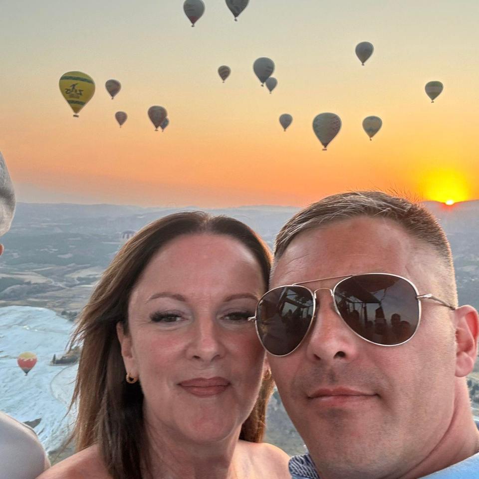 Couple in hot air balloon at sunrise with many hot air balloons in the sky.