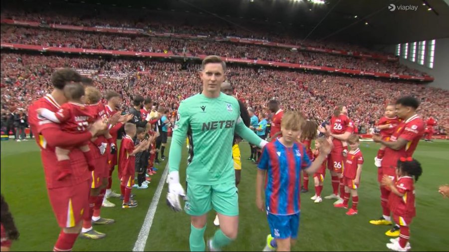 Goalkeeper walking onto a soccer field with children.