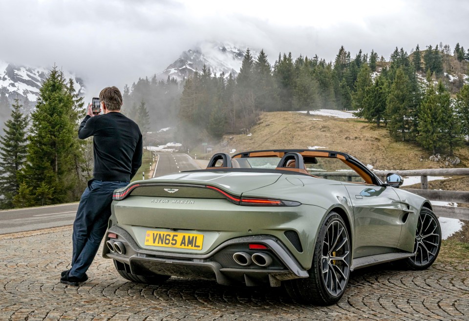 Aston Martin Vanta parked by a mountain road, a person taking a picture.
