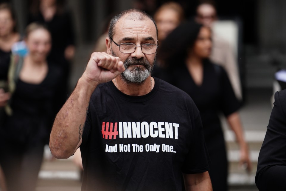 Andrew Malkinson, exonerated after 17 years in prison for a rape he did not commit, raises his fist.  His shirt reads "INNOCENT And Not The Only One."