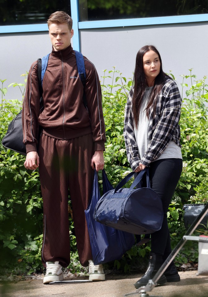 Lauren Branning and Peter Beale carrying bags on a film set.