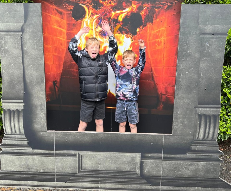 Two boys sticking their tongues out in front of a large fireplace photo cutout at Warwick Castle.