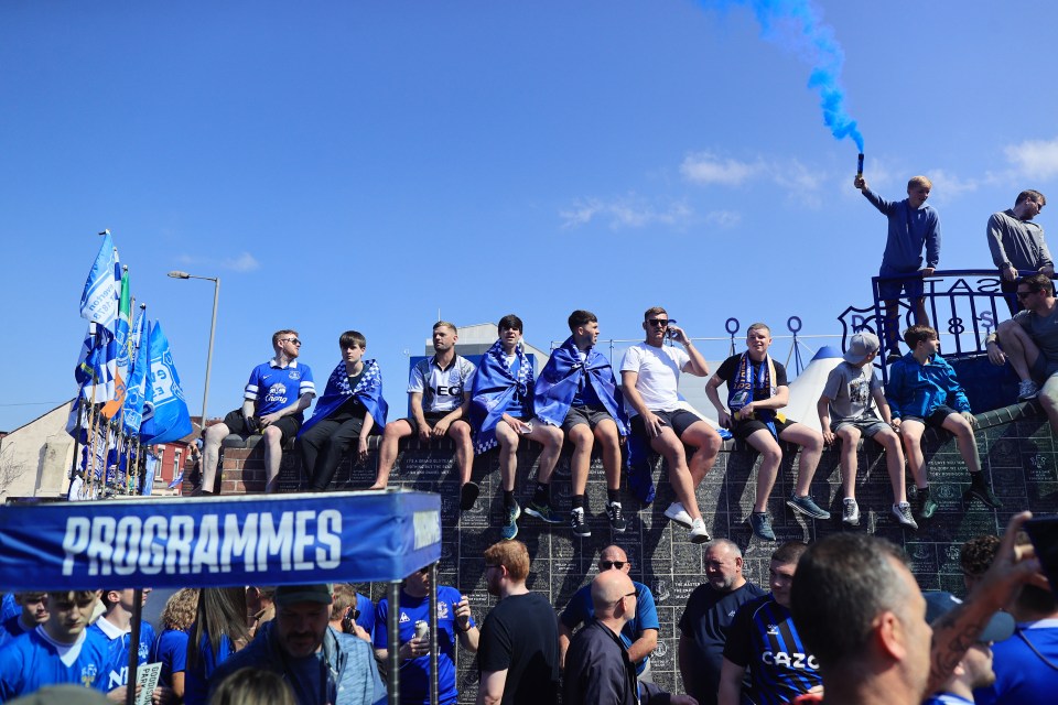 Everton fans sitting on a brick wall before a soccer match.