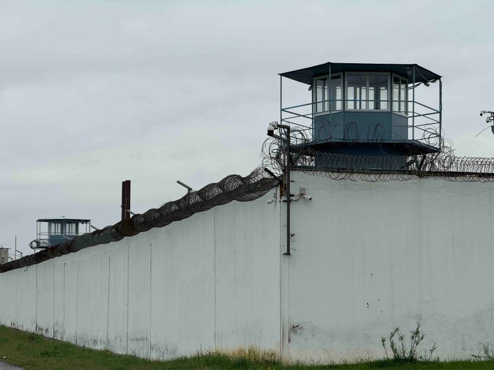 Exterior of a prison with a high wall, barbed wire, and guard towers.