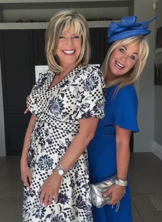 Two women at a garden party.  One woman wears a black and white floral dress; the other wears a royal blue dress and a blue hat.