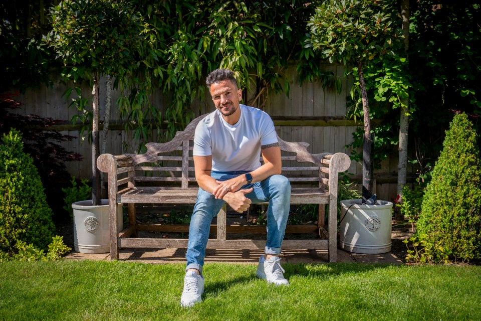 Peter Andre sitting on a wooden bench in his garden.