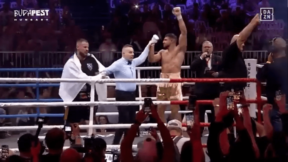 A boxer raises his arm in victory in a boxing ring.
