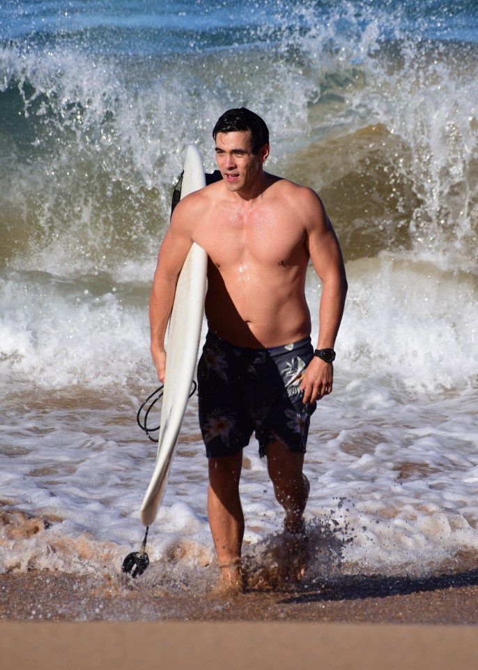 James Stewart carrying a surfboard out of the ocean.