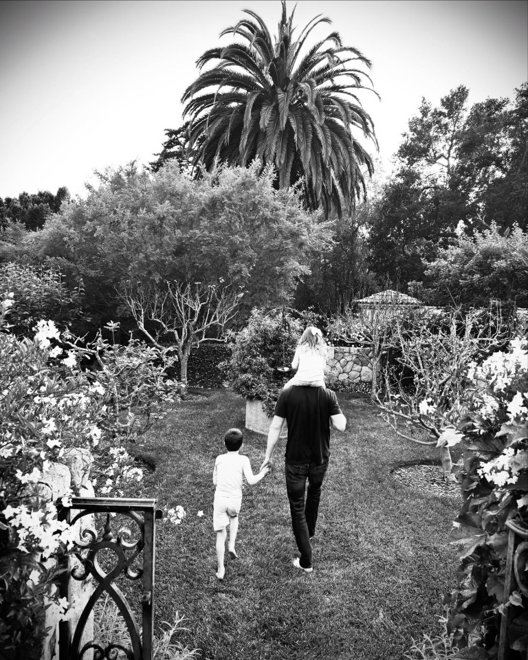 Black and white photo of a man walking with his two children in a garden.