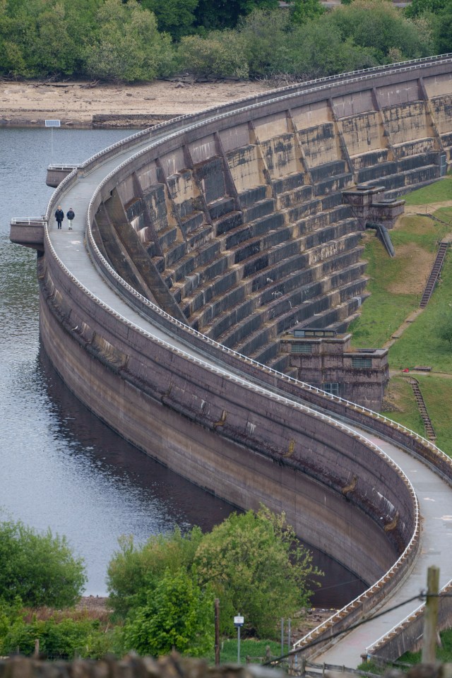 People walking along the curved dam wall of a reservoir during a drought.